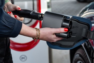 A person plugging a Tesla Supercharger plug into a Ford vehicle via the Ford NACS adapter.